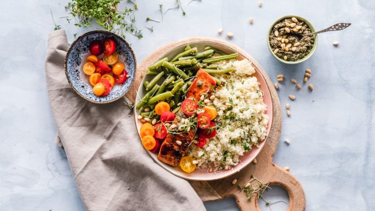 Bowl with salmon, green beans and grains beside cherry tomatoes