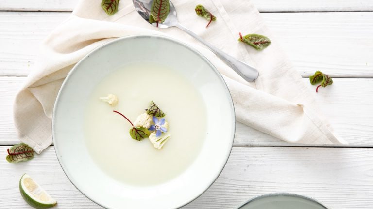 White creamy bowl with herbs on a white wooden table