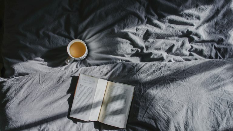 Open book and cup of tea on a bed