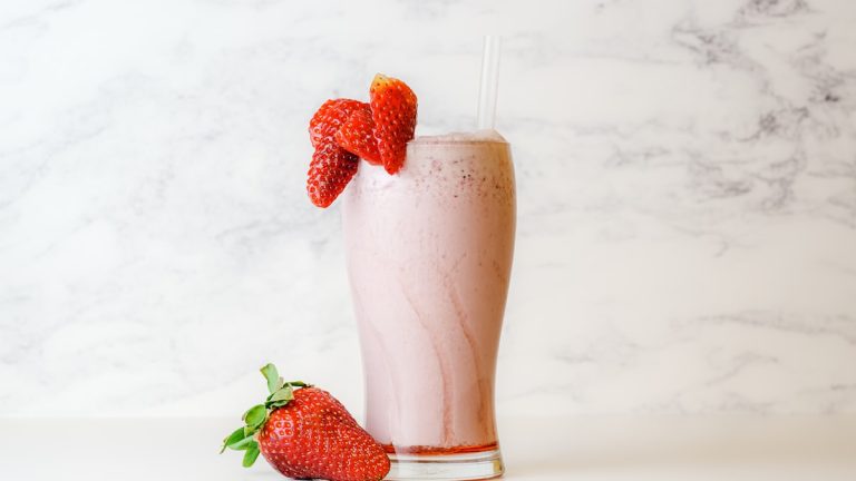 Pink berry smoothie in a tall glass with fresh strawberries