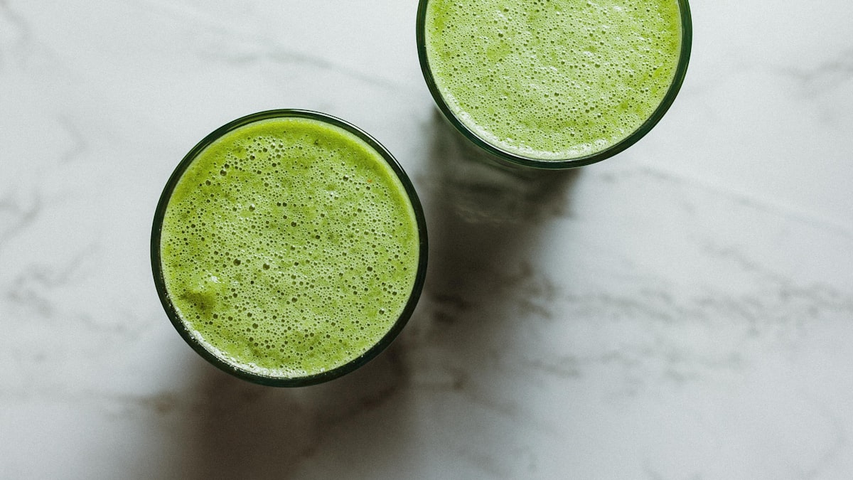 Two green protein smoothies on a white marble counter