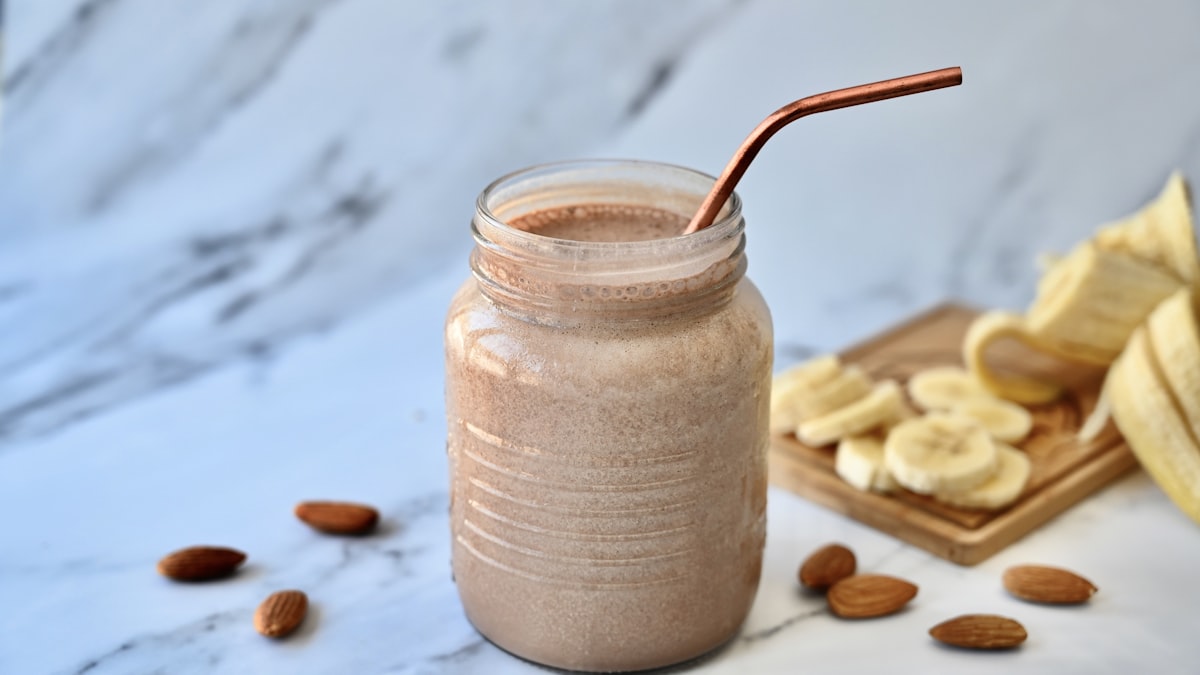 Peanut butter banana protein smoothie in a mason jar with banana slices and almonds