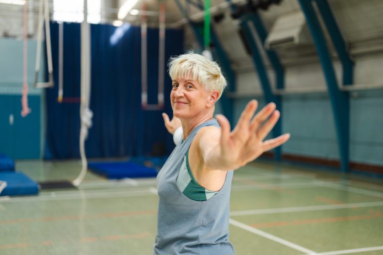 Older woman smiling in an exercise class with her arm outstretched