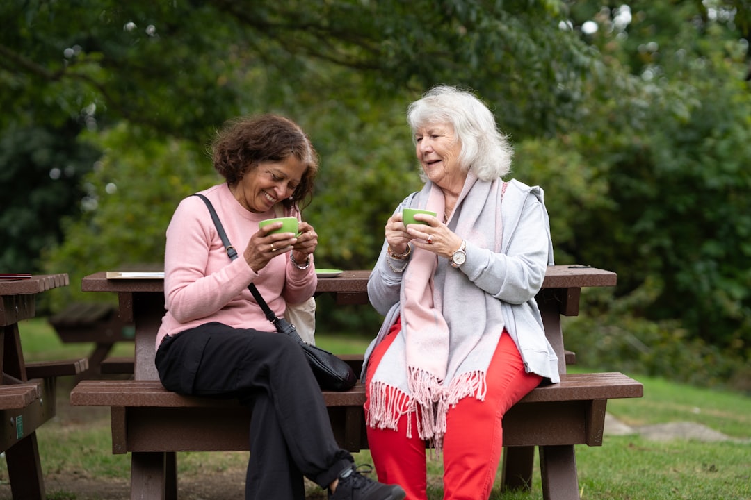 Two older women laughing together over mugs at a picnic table