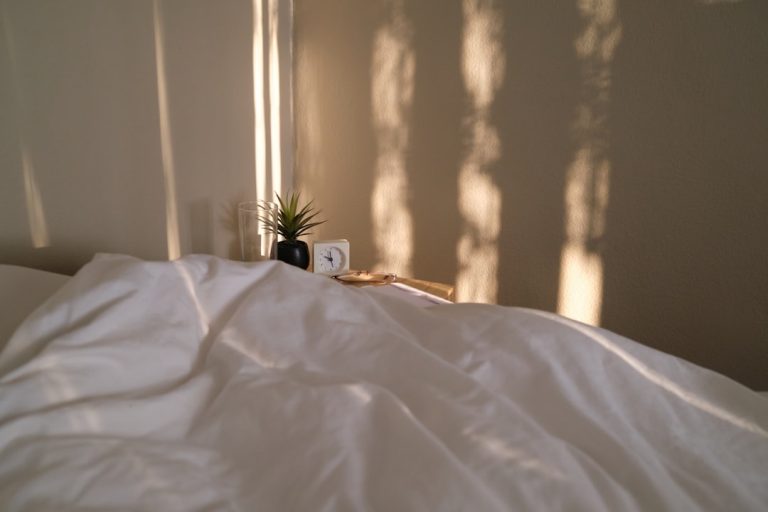 Bed with white bedding, a small alarm clock, and soft morning light