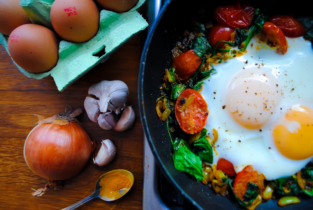Skillet of eggs cooked with tomatoes and spinach next to a carton of brown eggs