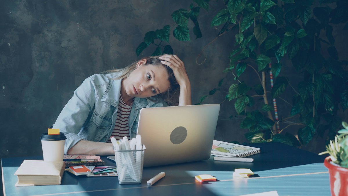 A woman at a laptop resting her head in her hand, looking worn out