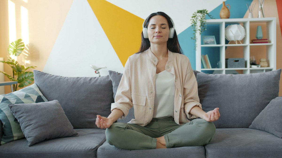 A woman meditating on her couch with headphones on