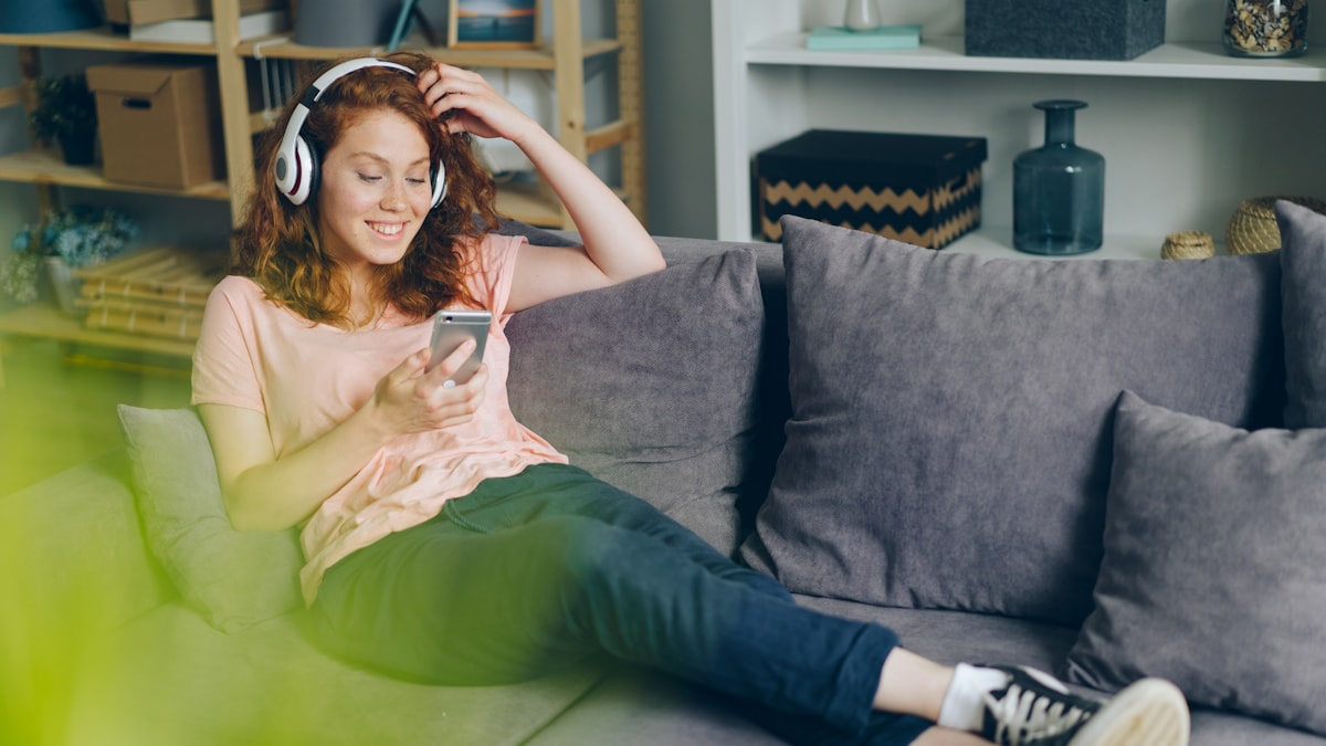 Woman relaxing on a couch with headphones and a phone