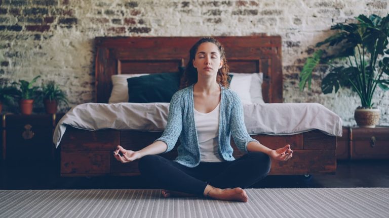 Woman meditating cross-legged on a bedroom floor