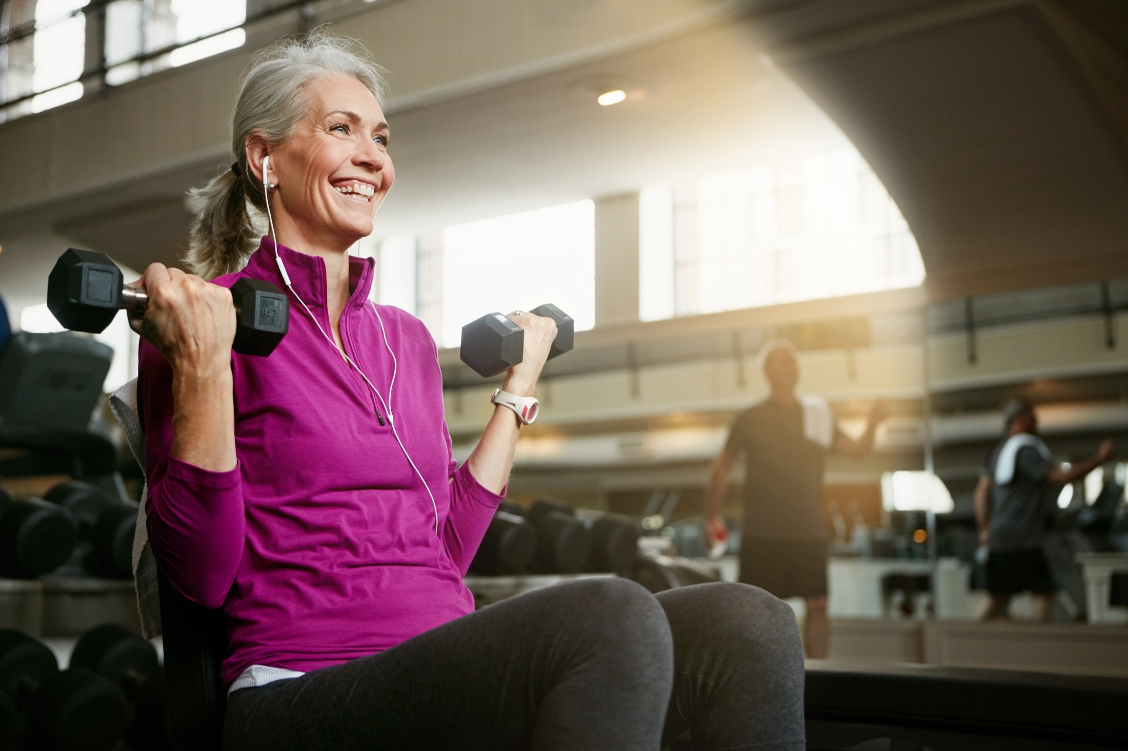 Smiling silver-haired woman lifting dumbbells at the gym