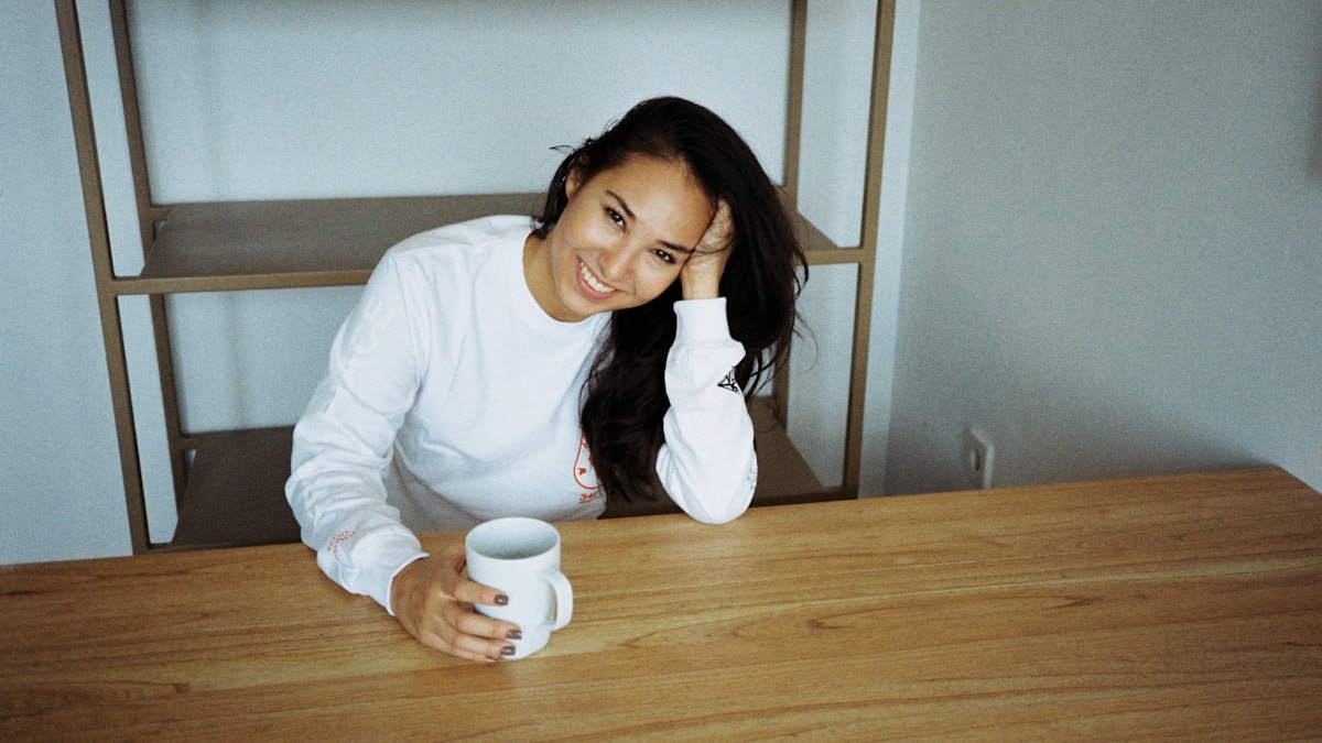 Woman sitting at a table with a mug, hand on her head