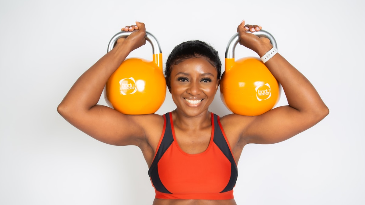 Smiling woman holding two kettlebells over her shoulders